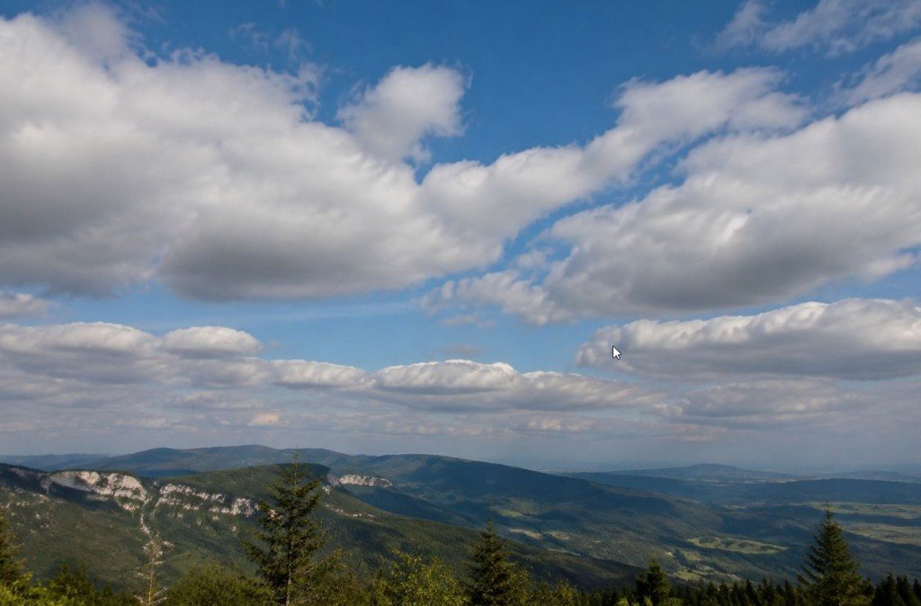 A wide mountain vista under a bright blue sky filled with scattered white cumulus clouds — the kind of cover that can hide an eclipse without warning.