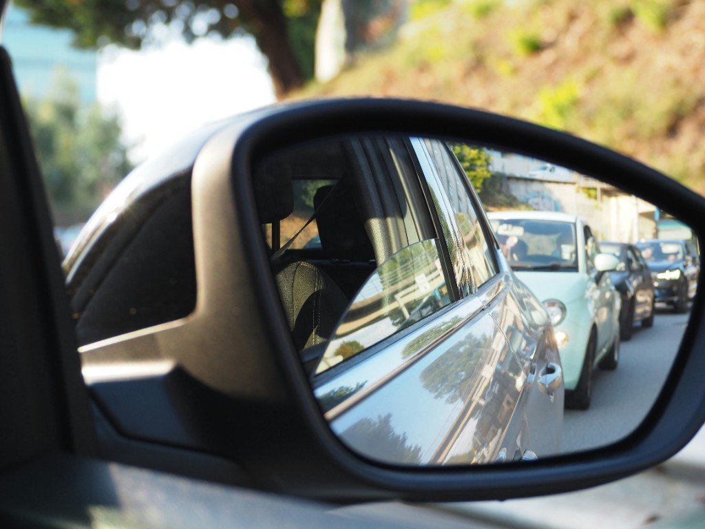 A line of cars reflected in a side mirror on a sunny road — eclipse-day traffic barely moving.