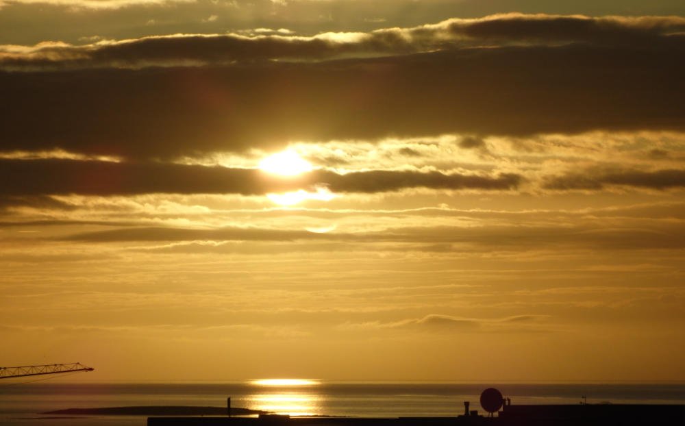 Golden sunset light breaking through cloud layers over a calm Icelandic harbour.