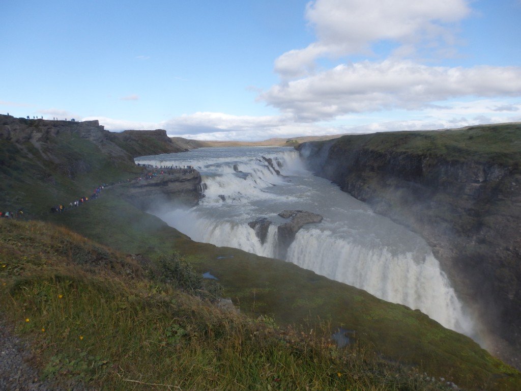 Gullfoss waterfall plunging into a deep canyon, with visitors on the cliff-top path for scale.