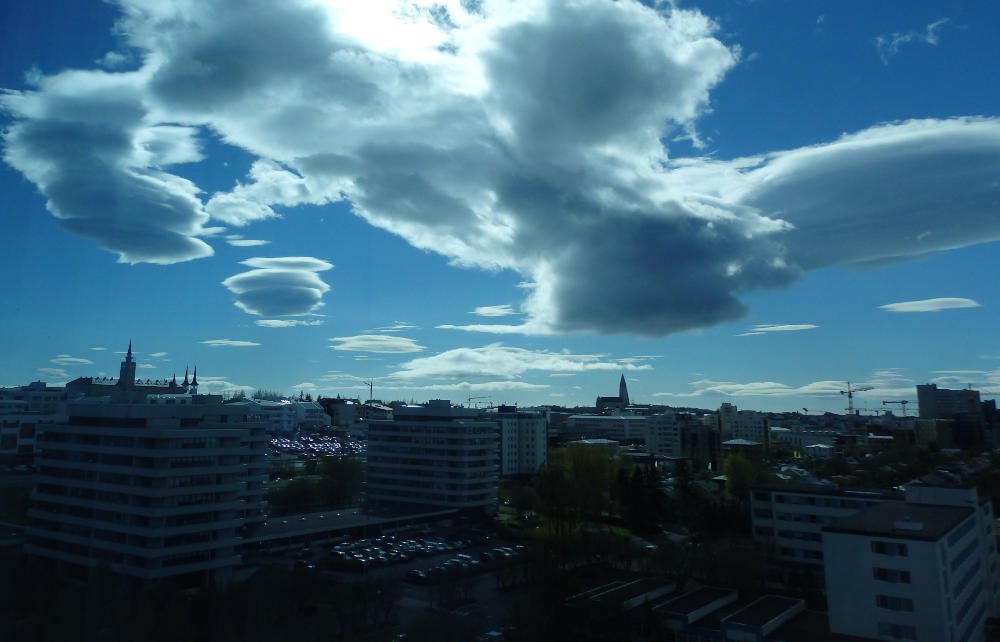 Reykjavik cityscape with Hallgrímskirkja spire under dramatic lenticular clouds and a bright sky.