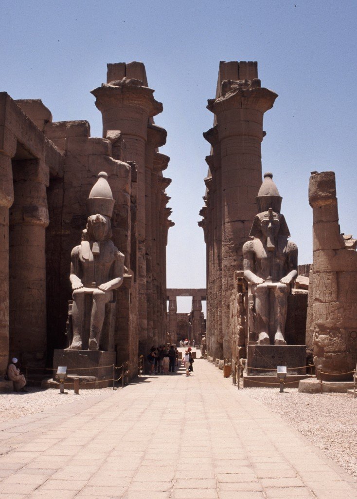 The colonnade at Luxor Temple with seated pharaoh statues and towering columns under a clear blue sky.