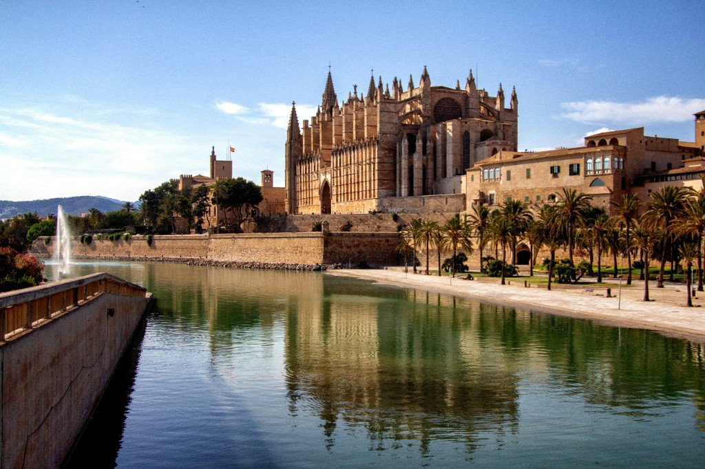 La Seu cathedral above the Parc de la Mar lake in Palma, with palms and a fountain in the foreground.