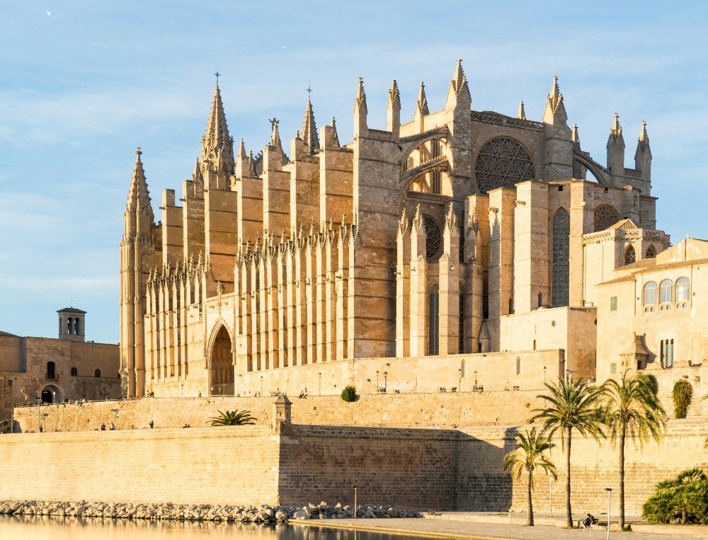 La Seu cathedral above the Parc de la Mar embankment, with palm trees and golden light on the sandstone.