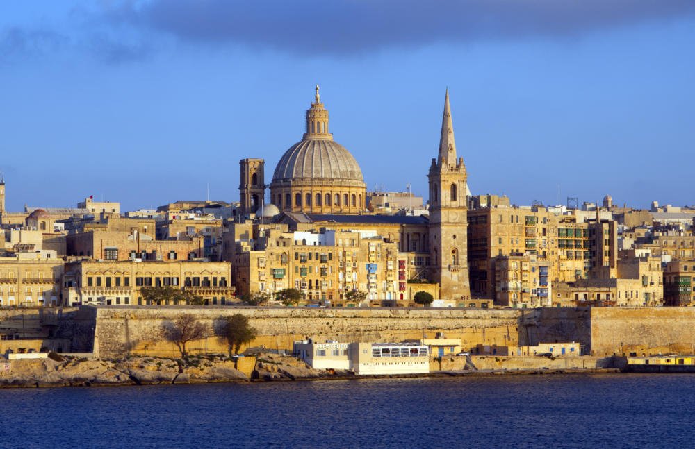 Valletta's golden limestone skyline across the Grand Harbour, with the dome of Our Lady of Mount Carmel and St Paul's Pro-Cathedral spire.