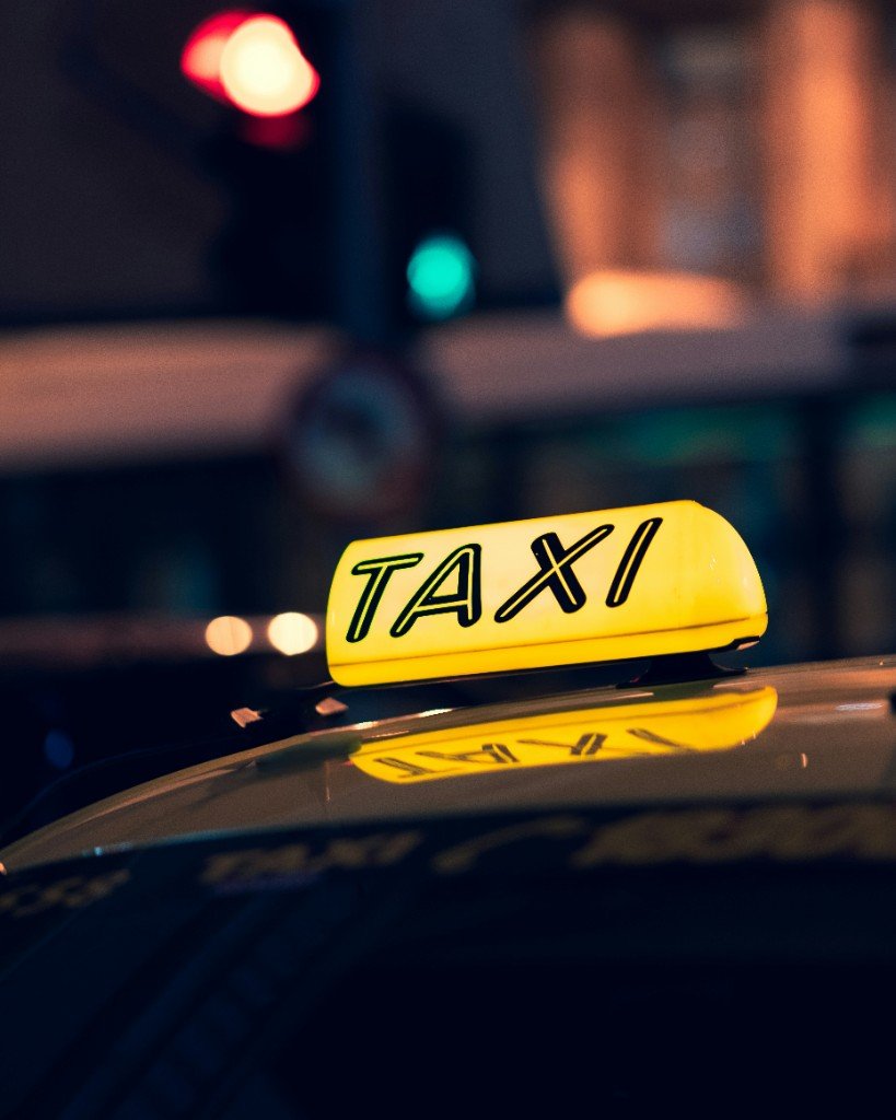An illuminated yellow TAXI roof sign on a car at night — check the vehicle and driver before you get in.